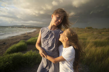 Blond mother and daughter hugging at windy beach - NJAF00971