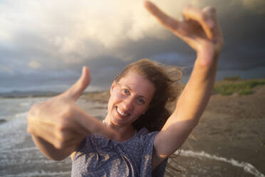 Happy blond woman enjoying sunset making finger frames at beach - NJAF00974