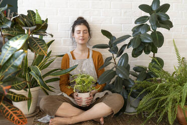 Woman with eyes closed sitting cross-legged amidst plants at nursery - VBUF00565