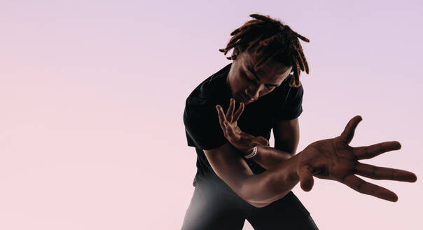 Rhythmic Gen Z male dances energetically in a studio, his expressive movements creating an artistic silhouette against a pink background. Using wireless earbuds, he listens to music and moves with passion. - JLPSF31677