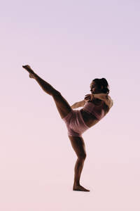 Professionelle Turnerin zeigt ihre Beweglichkeit und Geschicklichkeit in einer Übung, in der sie Flexibilität und Gleichgewicht zeigt. Mit einem durchtrainierten Körper posiert sie anmutig auf einem Bein und verkörpert die Kunst der Akrobatik. - JLPSF31689