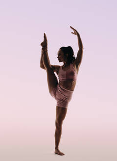 Woman displaying impressive skill in gymnastics while standing against a studio background, . Her lean physique, flexibility, and fitness clothing highlight her toned form performing an acrobatic pose. - JLPSF31690