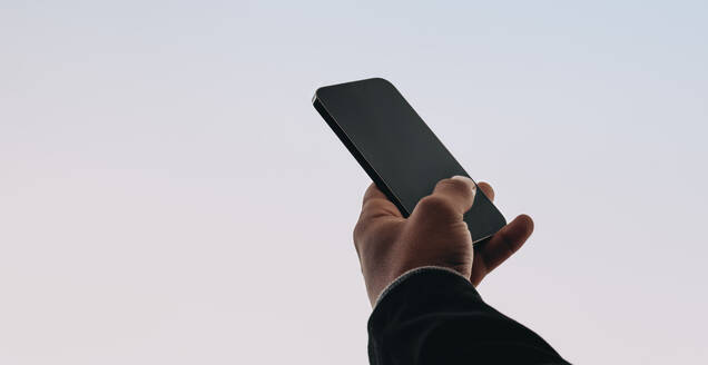 Male hand holds a modern smartphone displaying a social media message. The person is seen reading and texting, using a mobile app on the phone. The background is a studio, representing a connected and tech-savvy lifestyle. - JLPSF31705