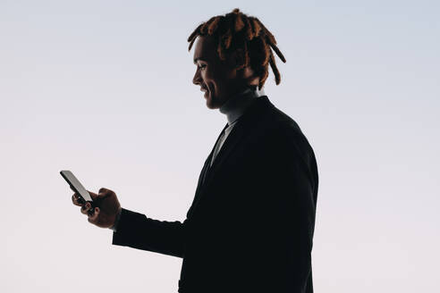 Happy man using a smartphone, reading and texting on a mobile app. Silhouette of a young man highlighting the modern lifestyle of seamless connection and communication against a studio background. - JLPSF31706