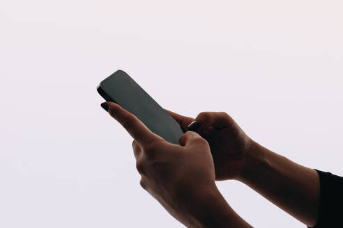 Female hands holding a smartphone in a studio, typing and scrolling a social media app. Woman connecting to the virtual world by engaging in text messaging and social networking. - JLPSF31768