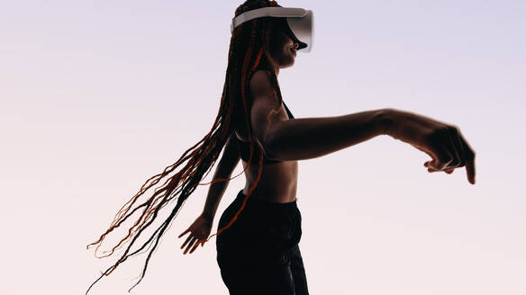 Eine selbstbewusste Frau mit Zöpfen tanzt in einem Studio und präsentiert ihren fitten Lebensstil. Mit einer VR-Brille genießt sie ein immersives und interaktives Erlebnis und bringt ihre fröhliche und energiegeladene Persönlichkeit durch Bewegung zum Ausdruck. - JLPSF31810