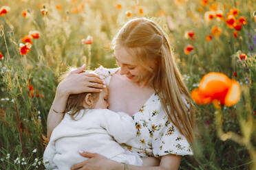 Smiling mother breastfeeding daughter in flower field - OLRF00236