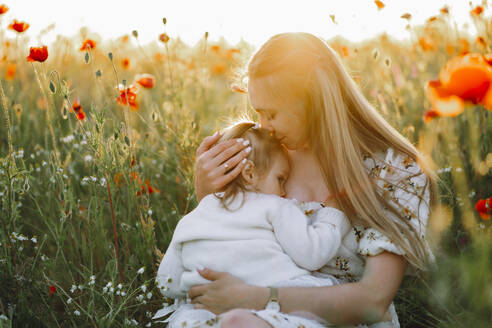 Mother kissing daughter and breastfeeding in flower field - OLRF00237