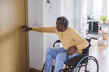 Senior man in wheelchair opening door at home - ALZF00166