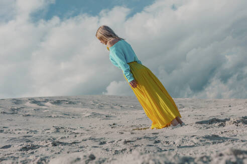 Woman wearing yellow skirt and bending under cloudy sky - VSNF01864