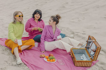 Stylish women sitting on tablecloth on picnic on sea coast, Poland - VSNF01877