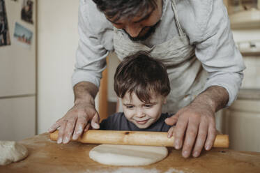 Father and son rolling dough in kitchen at home - ANAF02851