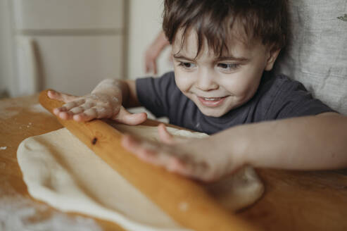 Smiling boy rolling dough in kitchen at home - ANAF02853