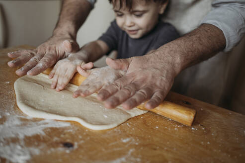 Father teaching son to roll dough in kitchen at home - ANAF02858