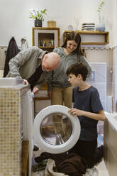 Senior man assisting grandchildren while doing laundry in bathroom at home - MASF43664