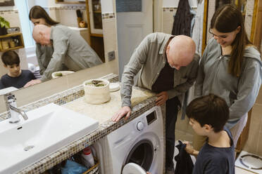 Senior man teaching grandchildren to use washing machine in bathroom at home - MASF43665