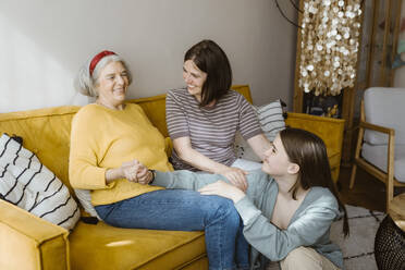 Happy senior woman spending leisure time with granddaughter and daughter-in-law while sitting on sofa at home - MASF43674