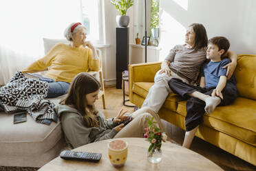 Mother and son talking with senior woman sitting on chair at home - MASF43711