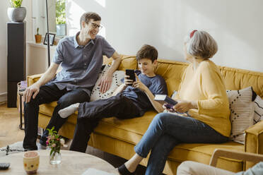 Happy man sitting on sofa with son and mother-in-law at home - MASF43714