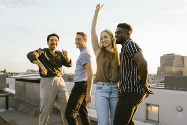 Carefree woman dancing with male friends on building terrace at sunset - MASF43789