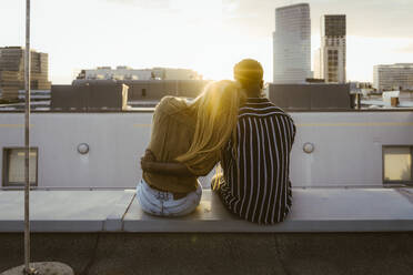 Rear view of multiracial couple sitting on terrace and looking at buildings in city - MASF43791