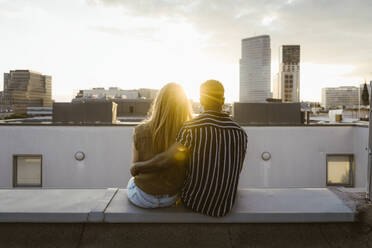 Rear view of boyfriend and girlfriend sitting on terrace and looking at buildings in city - MASF43792