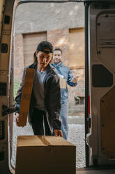 Male and female delivery coworkers unloading boxes from van trunk - MASF43837