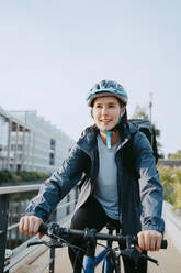 Smiling female delivery person wearing helmet and sitting on bicycle - MASF43849