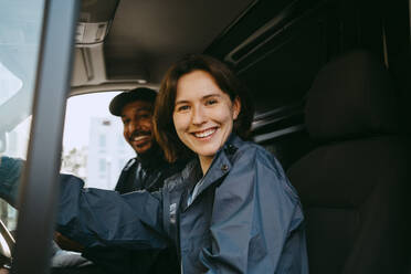 Portrait of happy male and female delivery coworkers sitting in van - MASF43868