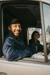 Portrait of smiling male delivery person sitting with female colleague in van - MASF43869