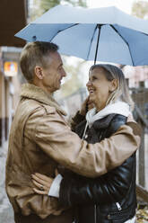 Side view of romantic mature couple standing under umbrella at street - MASF43990