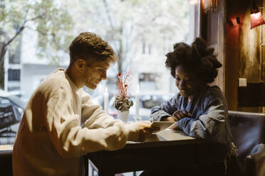 Multiracial couple going through menu card while sitting at table during date at bar - MASF44010