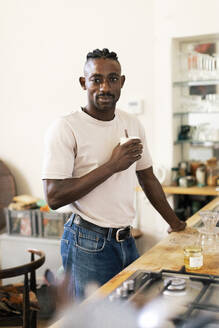 Portrait of male owner having coffee while standing in workshop - MASF44122