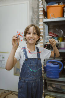 Porträt einer lächelnden Schülerin, die einen mit Drähten verbundenen Elektromotor in einem Technik-Workshop in der Schule hält - MASF44170