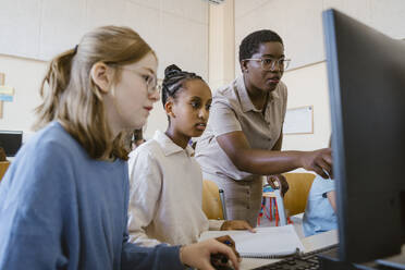 Female teacher explaining students over computer in classroom at school - MASF44178