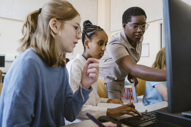 Female teacher pointing at computer while teaching students in classroom at school - MASF44179