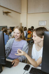 Smiling boy talking to female friend using computer while sitting in classroom at school - MASF44202