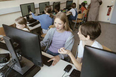 High angle view of male and female classmates discussing while sitting in computer class at school - MASF44203