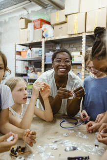 Porträt einer lächelnden Lehrerin mit Schülern, die in einer Werkstatt in der Schule mit elektrischen Bauteilen arbeiten - MASF44221