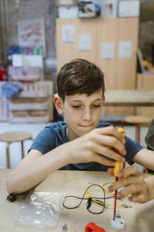 Junge zieht Schraube an elektrischem Teil mit Schraubenzieher auf Tisch in Werkstatt in Schule an - MASF44230