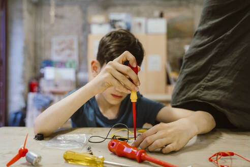 Junge lernt in der Schulwerkstatt, ein elektrisches Bauteil mit einem Schraubenzieher zu reparieren - MASF44231