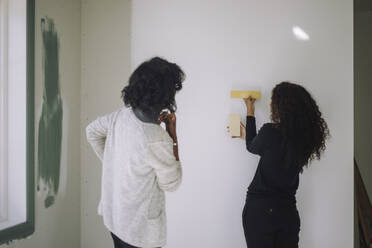 Female architect showing wall paint samples to client while standing at under construction apartment - MASF44253