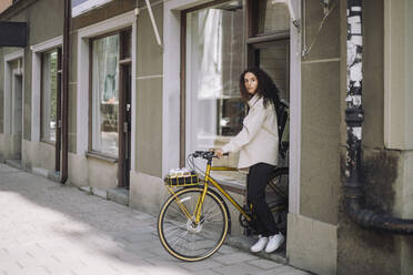 Seitenansicht eines weiblichen Designers, der beim Verlassen des Büros mit dem Fahrrad wegschaut - MASF44299