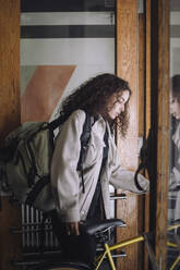 Female architect carrying backpack while leaving with bicycle from building - MASF44308