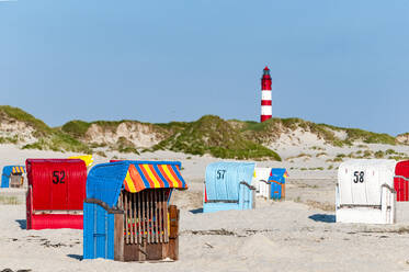 Deutschland, Schleswig-Holstein, Amrum, Strandkörbe mit Kapuze am Sandstrand mit Leuchtturm im Hintergrund - EGBF01077