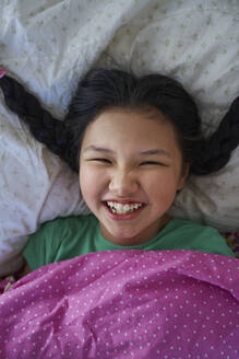 USA. NY, Cute happy carefree girl with long braids relaxing on a bed - AZF00604