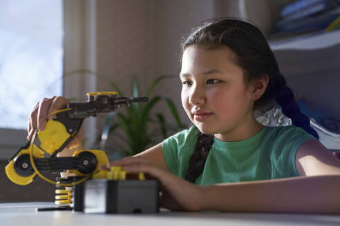 USA. NY, Cute carefree girl at home studying robotic arm at table - AZF00609
