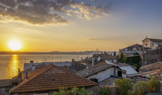 Italy, Lazio, Anguillara Sabazia, Rooftops of houses overlooking lake Bracciano at sunset - MAMF03032