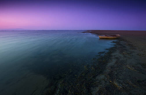Eine heitere Abenddämmerung legt sich über das Ebro-Delta, und ein einsames Boot ruht bei Ebbe auf dem blau-violett gefärbten Wasser - ADSF54948