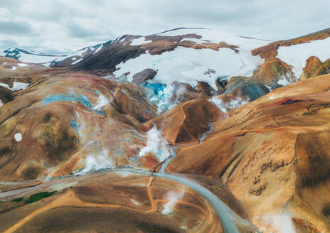 Luftaufnahme, die die leuchtenden Farben und den Dampf des geothermischen Geländes in Island mit Schneeflecken und einem kurvenreichen Weg einfängt. - ADSF55030